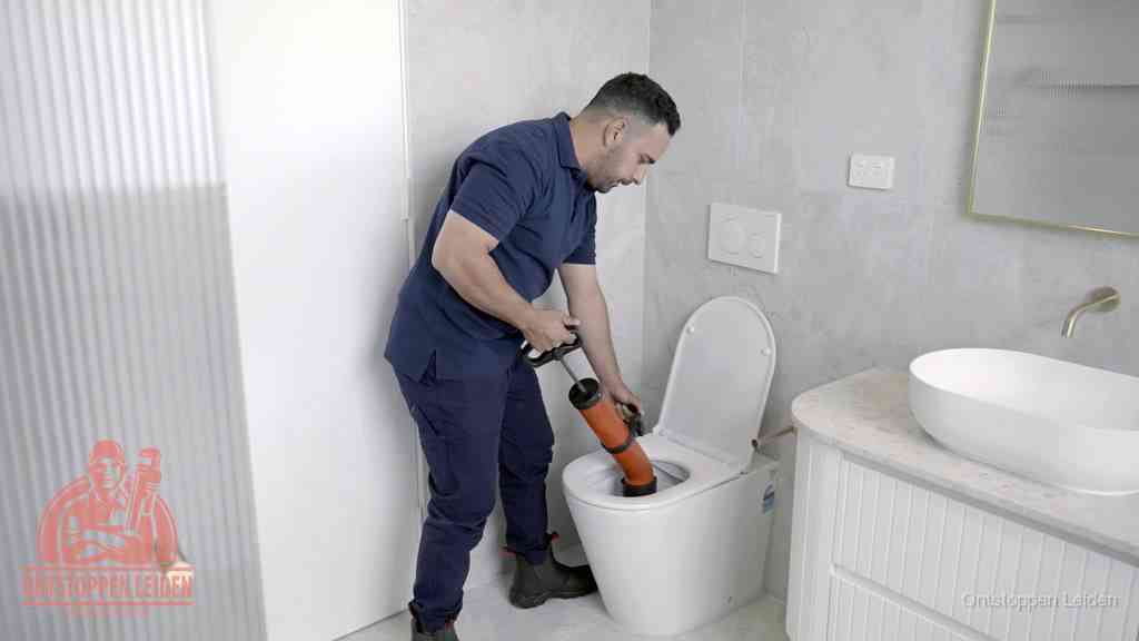 Een monteur buigt over een wandcloset en duwt met de hand een persluchtontstopper in de toiletpot om de verstopping handmatig los te maken in Leiden