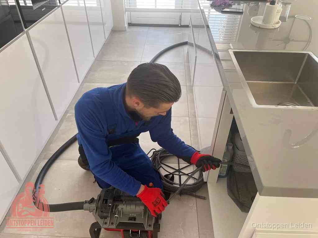 Een monteur ontstopt de keukenafvoer onder de spoelbak met een elektrische veermachine in Leiden