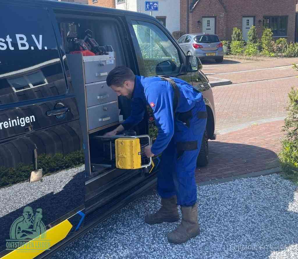 Een monteur pakt buiten op de oprit gereedschap uit de bedrijfsbus, het moment om een professional in te schakelen voor een verstopte afvoer in Leiden