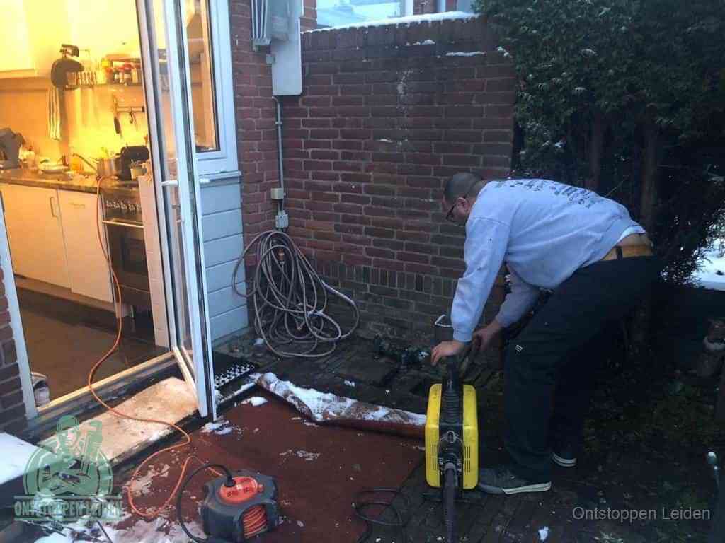 Een monteur werkt buiten bij een open riool-/grondput met een elektrische ontstoppingsmachine om een verborgen afvoerprobleem op te sporen in Leiden
