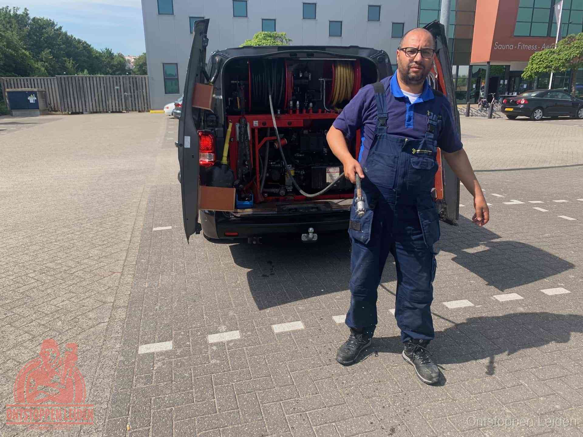 Een monteur bij zijn bestelbus met een hogedruk- en rioolreinigingsunit, klaar om de oorzaak van terugkerende wc-verstoppingen aan te pakken in Leiden