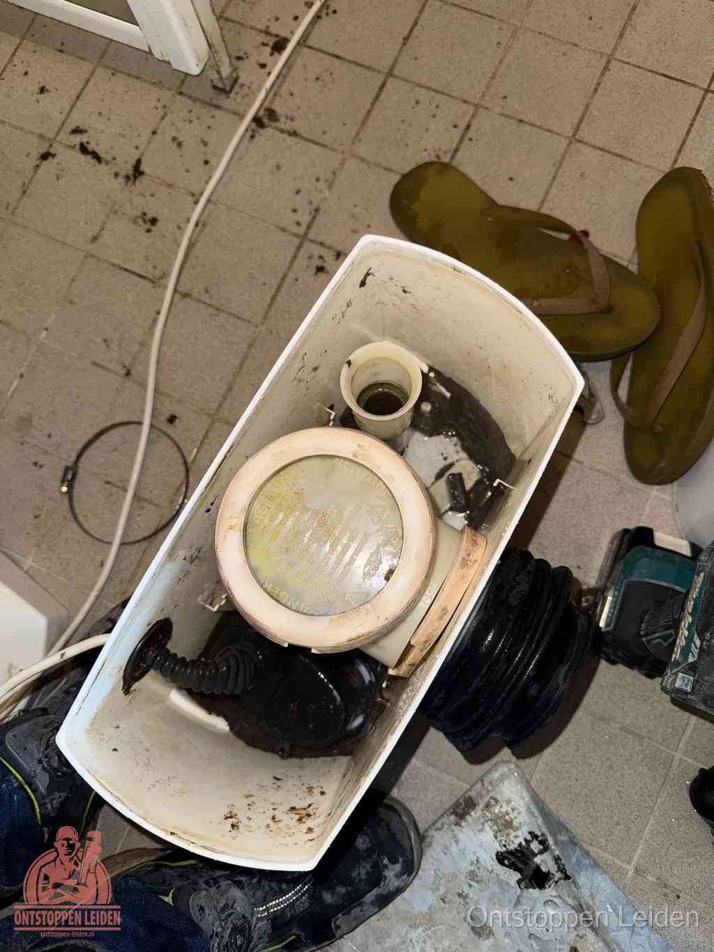 Een gedemonteerde toiletpot op de vloer met ontstoppingsveer en gereedschap ernaast, het verwijderen van een vastzittend voorwerp uit de wc in Leiden