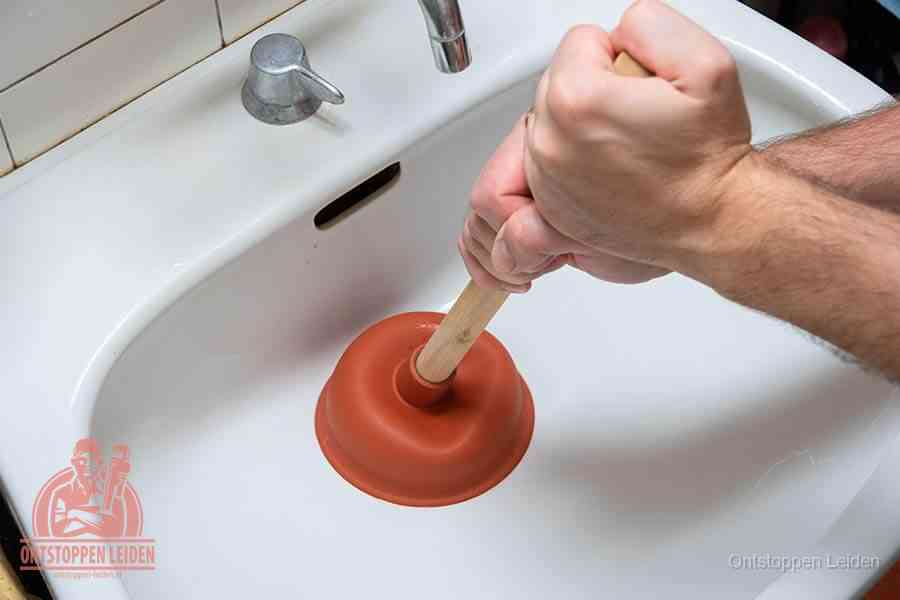 Twee handen gebruiken een rode rubberen plopper op een sanitair-afvoer om het toilet te ontstoppen in Leiden