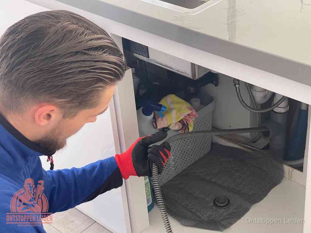 Een monteur voert een flexibele ontstoppingsveer in de afvoer om een verstopping voorbij de bocht van het toilet te bereiken in Leiden