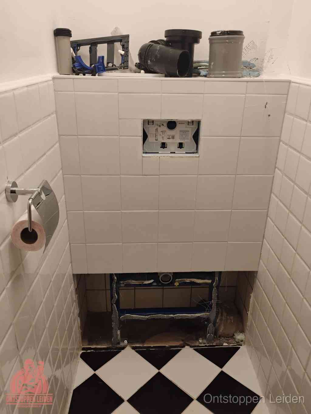 Een toiletruimte waar het hangtoilet en de inbouwreservoir-onderdelen zijn vrijgelegd voor onderhoud, periodiek nazicht voorkomt een wc-verstopping in Leiden