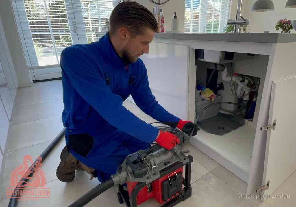 Een monteur voert een professionele elektrische ontstoppingsmachine in de afvoer onder de spoelbak tijdens het gootsteen ontstoppen in Leiden