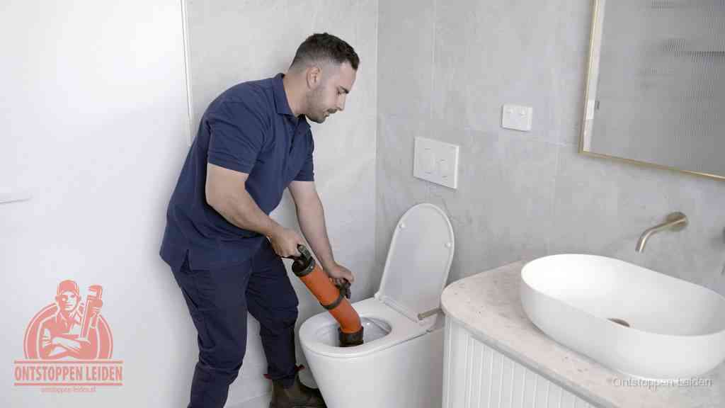 Een man gebruikt een handmatige luchtdruk-ontstopper in een modern betegeld toilet om zelf de wc te ontstoppen in Leiden
